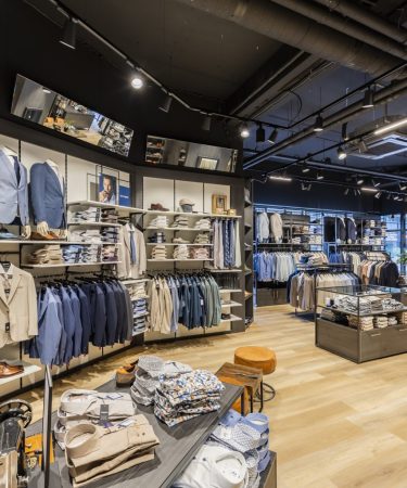 Winkelinterieur met sfeervolle verlichting, houten vloer en strakke wandpresentatie van kleding.
