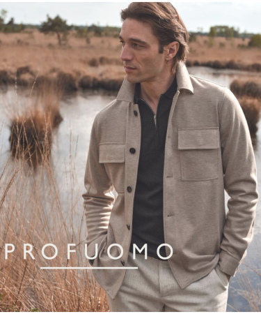 Man draagt een licht overshirt en lichte broek, staand bij water en riet in een open natuurlandschap.