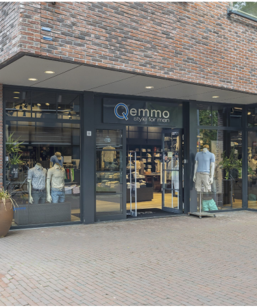 Gevel van Qemmo herenmodewinkel met glazen pui, etalagepoppen en overzicht van het interieur.
