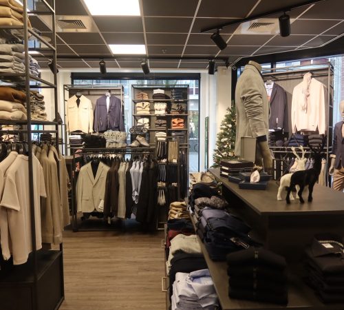 Extra kledingpresentatie met netjes gevouwen items en opgehangen outfits, passend binnen de moderne winkelstijl.