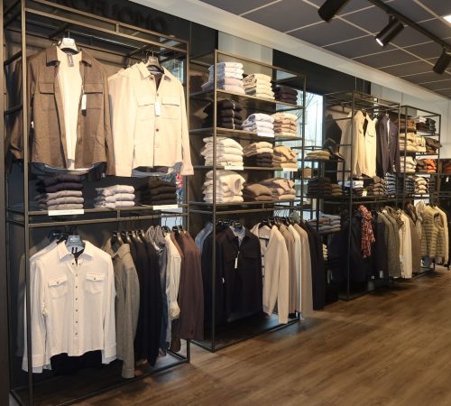 Rekken vol met zorgvuldig opgehangen overhemden, truien en jassen in neutrale en stijlvolle kleuren.