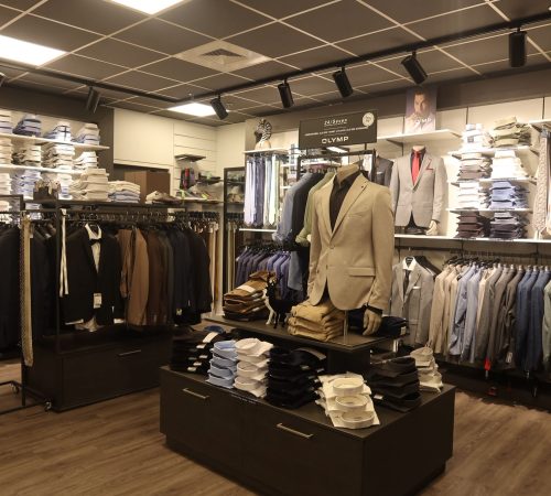 Binnenaanzicht van Qemmo met houten vloer, nette kledingrekken en sfeervolle verlichting. Diverse herenmode overzichtelijk gepresenteerd.